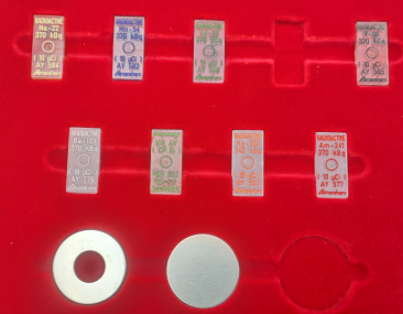 Foto eines Sets mit punktförmigen, in rechteckige Plastikmatrizen eingebetteten, und von flachen, runden Kalibrierstrahlern.